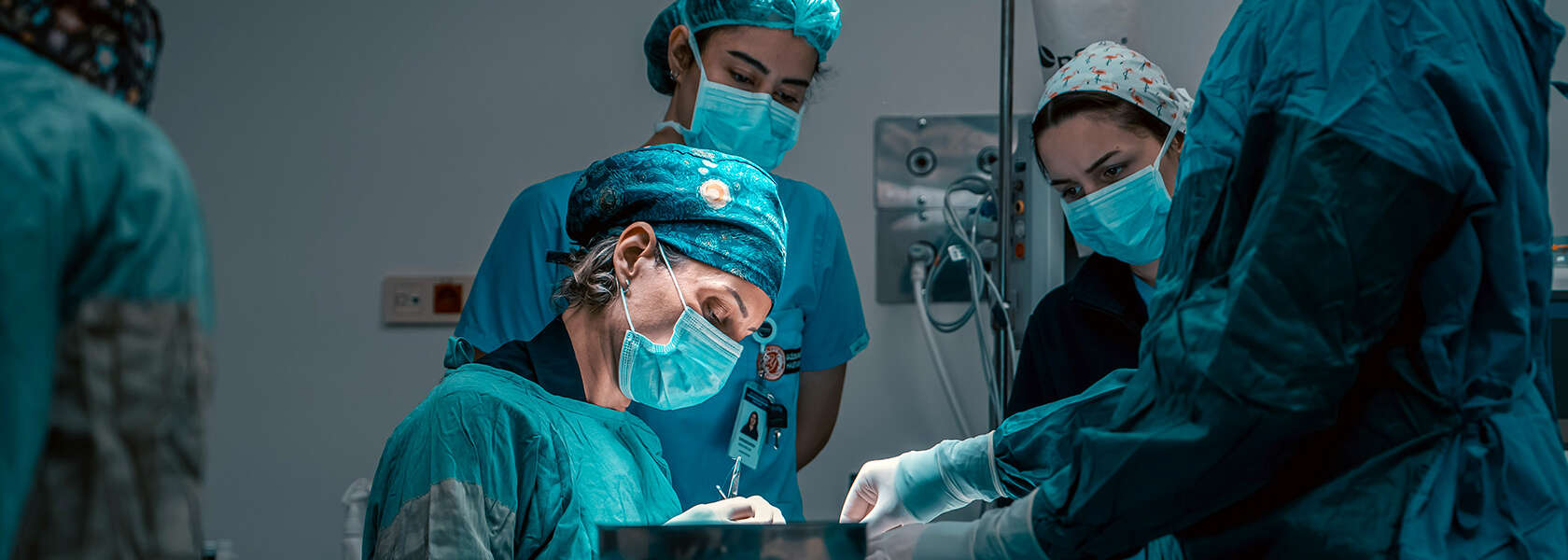 people in masks and surgical gear hold instruments over a table